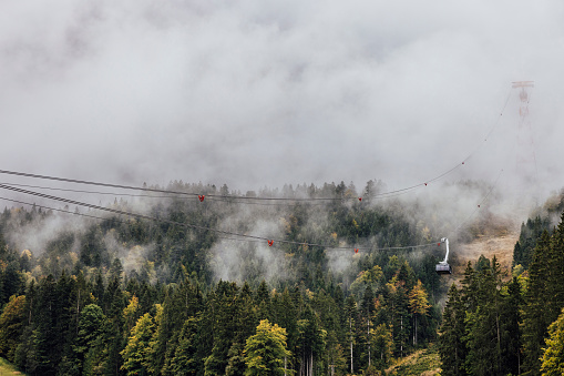 A drone shot of the beautiful scenery in Garmisch-Partenkirchen, Germany. There is a woodland with a cable car running through it and the clouds are enveloping the cable car power lines.