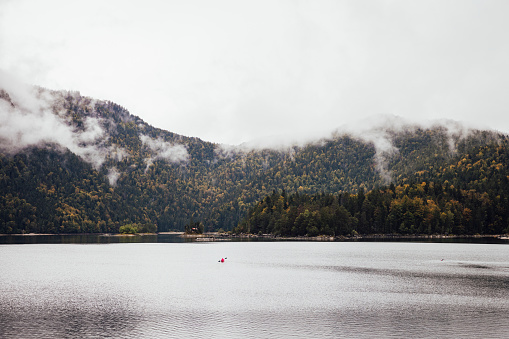 Lake Eibsee in Garmisch-Partenkirchen, Germany. The lake is surrounded by woodlands and mountains which the clouds are covering slightly. There is someone kayaking in the lake.