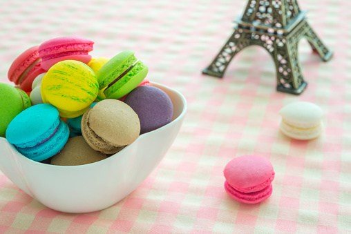 Colorful France macaroons in white bowl and pink plaid tablecloth background copy space. French food, culture, food design concept.