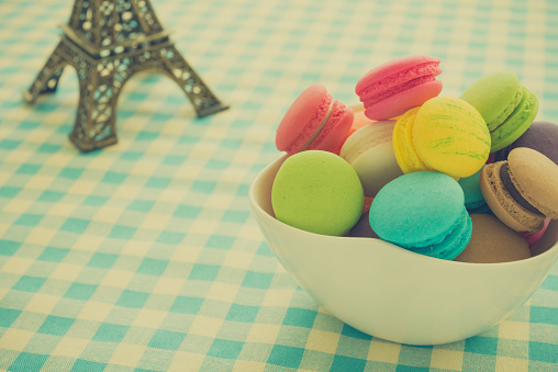 Colorful France macaroons in white bowl and blue plaid tablecloth background copy space. French food, culture, food design concept.