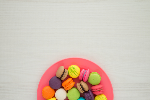 Colorful France macaroons on red plate with white table background copy space. French food, culture, food design concept.