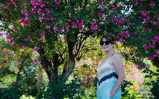 portrait of attractive mature woman with sunglasses in front of a tree with mauve flowers,space copy
