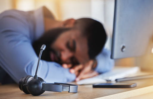 Call center, tired and man sleeping with microphone at desk for burnout, fatigue and low energy in telemarketing office. Closeup, stress and business consultant taking a nap at table in sales agency