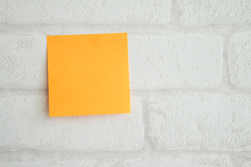 Yellow adhesive paper note on white brick wallpaper background with copy space. Office stationary, communication, information message concept.
