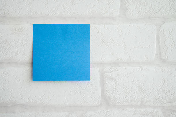 Blue adhesive paper note on white brick wallpaper background with copy space.