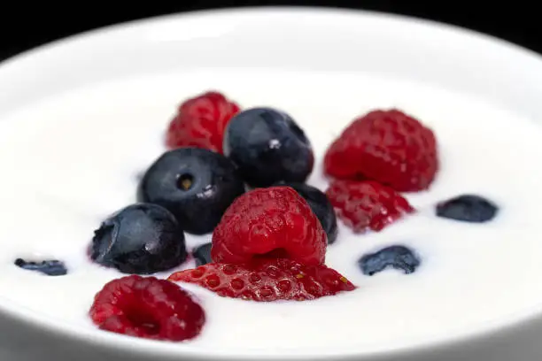 Photo of Close-up of a bowl with natural white yogurt and fresh raspberries, blueberries, strawberries, macro photography. Delicious healthy breakfast