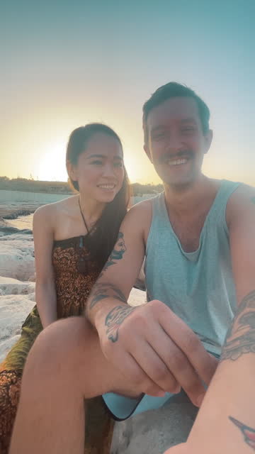 Smiling Japanese woman and her male best friend taking a selfie photo on the beach