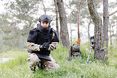 A man in a military uniform and a bulletproof vest works in the forest to demine the territory. A man puts on a protective helmet before starting work