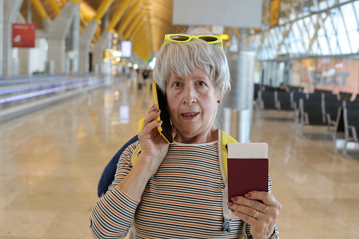 A very stressed looking senior female traveler is getting upsetting news on the phone. She opens her mouth while walking through the terminal.