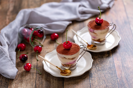 Traditional Italian dessert tiramisu with cherries in a glass