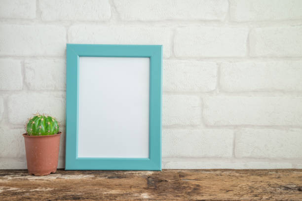 istock Blue photo frame on old wooden table with cactus over white brick wallpaper background. 1620655659