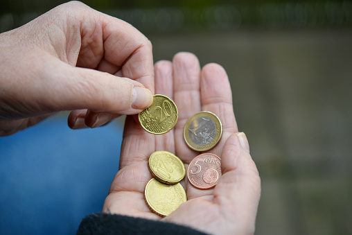 Poverty and inflation concept: Overhead view of an elderly woman with dirty fingernails counting some euro coins in her hand - selective focus, copy space
