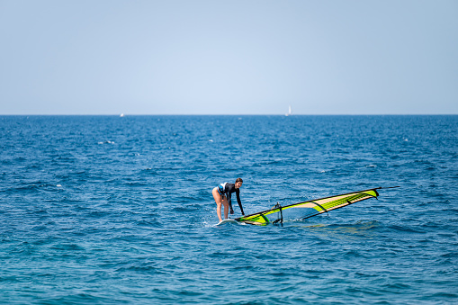 Young girl pulling a sail from the water before windsurfing in a blue ocean in a summertime.