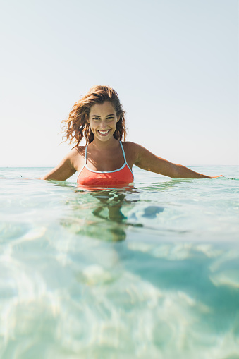 Young beautiful woman bathes in the sea. She is smiling and looking at camera.