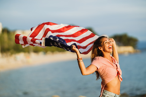 Smiling young woman with American national flag having fun and spending the day on the beach.