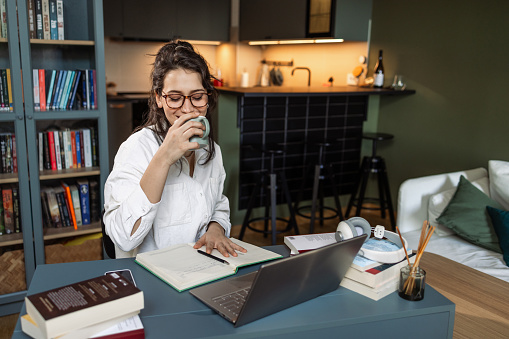 Young woman drinking coffee while working in a cozy environment at home