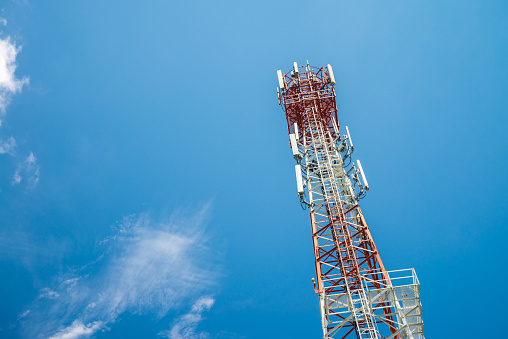 Red white telecommunication tower against blue sky background in sunny day from bottom view. Technology communication, internet, mobile network concept.