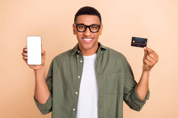 istock Portrait of clever successful handsome man demonstrate smartphone touchscreen debit plastic card isolated on beige color background 1620710237