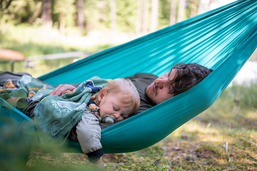 Father and baby son sleeping in a hammock on camping vacation.They are relaxing in nature.