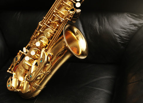 Alto sax on an armchair made of black leather. Plenty of copy space.
