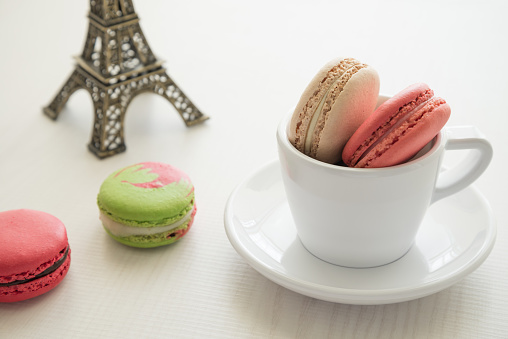 Colorful France macaroons in cup on white wood background copy space. French food, culture, food design concept.