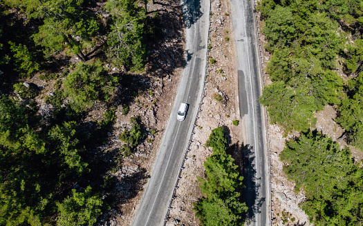 Mountainous region covered with pine forest.A bird's-eye view shot with drone.Vehicle driving on asphalt road.Nature road landscape