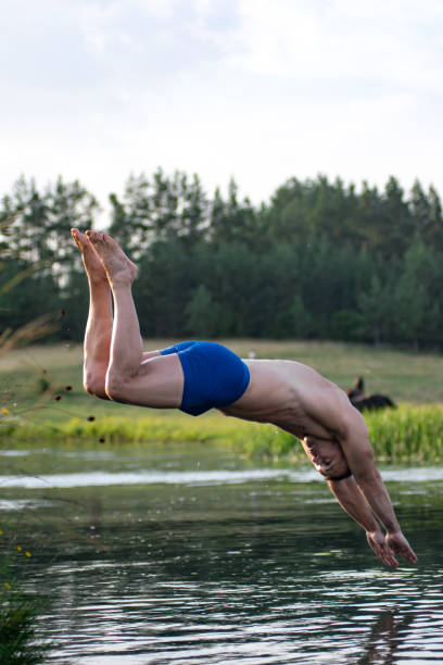 파란 수영복을 입은 남자가 여름 더위에 작은 강으로 뛰어든다 - relaxation muscular build simple living rural scene 뉴스 사진 이미지