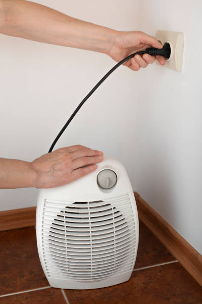 istock Female hand plugging space fan heater into wall power socket 1620790431