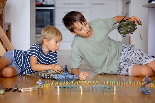 Happy children, siblings, boy, playing with tanks and soldiers at home. Beautiful kids playing with plastic toys