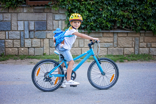 Cute child, boy with helmet and backpack, riding bike at the evening in rural nature, summertime