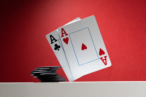 A pair of aces are balancing over the table, next to a stack of poker chips.  On a red background, copy space