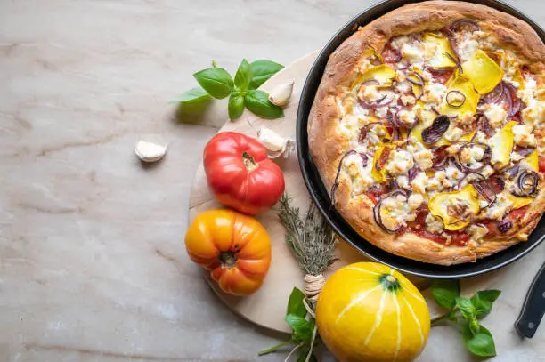 Zero waste food with a delicious homemade pizza. With fresh vegetables such as, onions, yellow squash, tomatoes from the garden. Baked with greek feta cheese and spanish duroc salami. Top view with copy space for concepts.