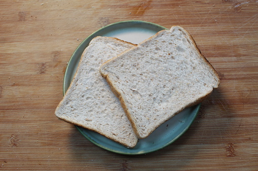 A photo of two pieces of bread on a plate on a wooden cutting board.