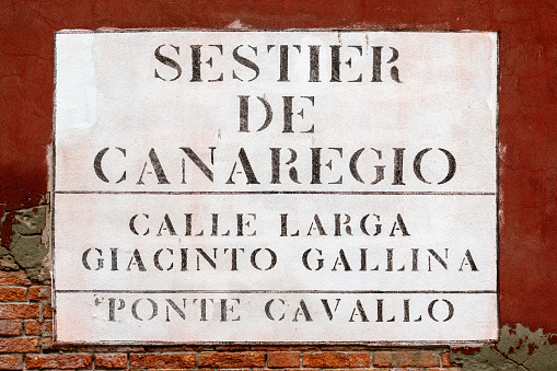 Street nameplate in Venice neighborhood or sestriere of Cannaregio, painted or sprayed in stencil type on dark red wall