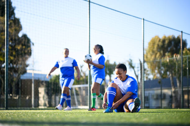 Woman tying shoelace sitting on football pitch Female football team practicing together on community sports grounds transgender-athletes stock pictures, royalty-free photos & images