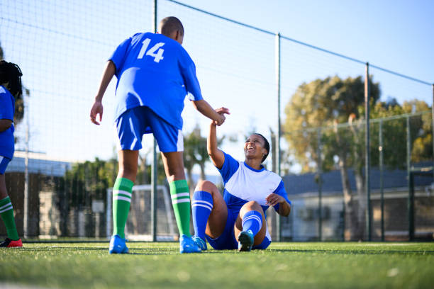 Young woman gives team mate a helping hand Female football team practicing together on community sports grounds transgender-athletes stock pictures, royalty-free photos & images