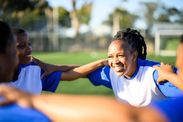 Candid portrait female football players huddled together Female football team practicing together on community sports grounds transgender-athletes stock pictures, royalty-free photos & images