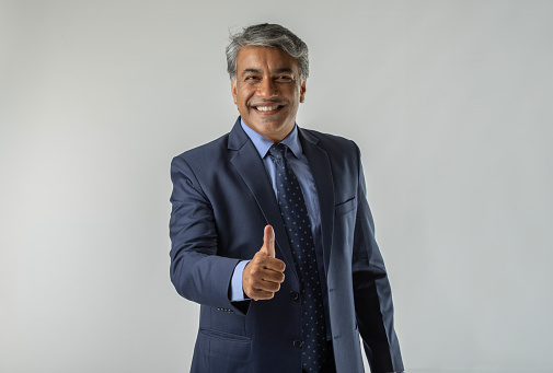 Portrait of confident positive senior businessman showing thumbs up gesture while standing against white background