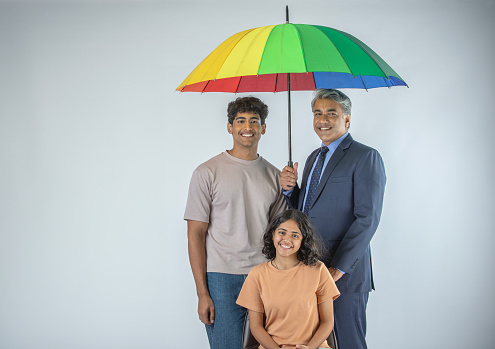 Smiling senior businessman holding umbrella while standing with son and daughter against white background