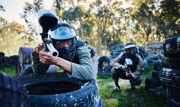 team, paintball and tires for cover, hiding or protection while firing or aiming down sights together in nature. group of paintballers waiting in teamwork for opportunity to attack or shoot in sports - paintballing violence exercising sport imagens e fotografias de stock