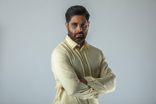 Portrait of confident mid adult businessman wearing eyeglasses with arms crossed standing against white background
