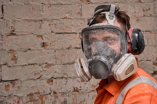 Construction worker wearing full face respirator mask and ear defenders for working in hazard environment.