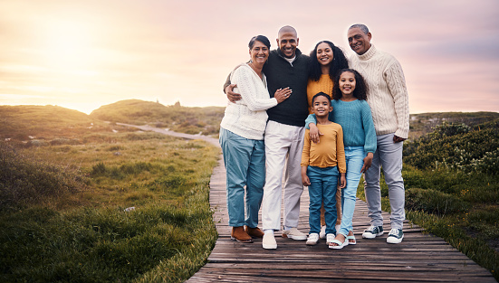 Happy family, portrait and people on vacation or holiday smile on a boardwalk and embrace together during sunset. Trip, getaway and grandparents with parents and children or kids bonding