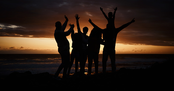 Freedom, sunset and silhouette of people at the beach while on a summer vacation, adventure or weekend trip. Carefree, happy and shadow of group of friends having fun together by the ocean on holiday