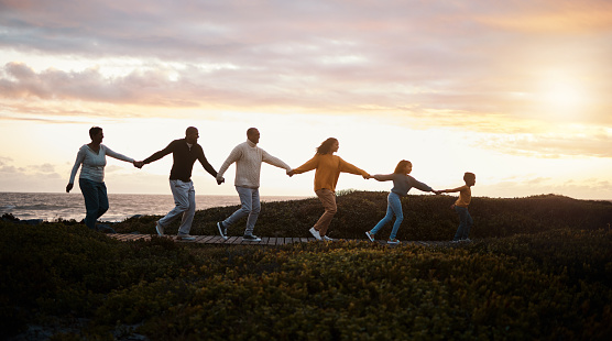 Family holding hands and walking in nature for group support, growth development and adventure together in sunset. Children with grandparents for fitness, health and running by a park path or ocean