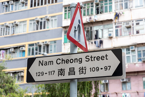 Pedestrians on or crossing road ahead sign and Nam Cheong Street sign in Hong Kong.