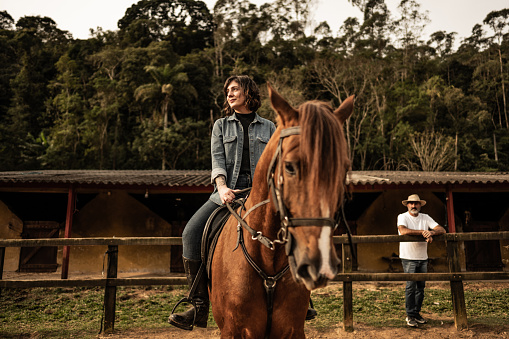 Young woman horseback riding and looking away contemplating on a stable