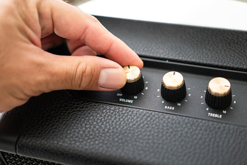 Action of a human hand is adjusting the volume dial wheel of the luxury designed music speaker   to start listening the music. Close-up and selective focus.