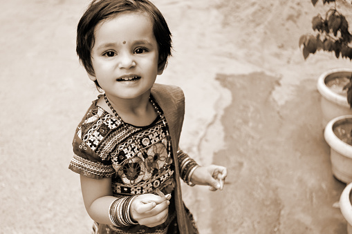 Portrait of small baby girl standing with pots near house.
