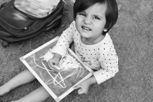 Cheerful baby girl of Indian ethnicity sitting in grass and showing the drawing.